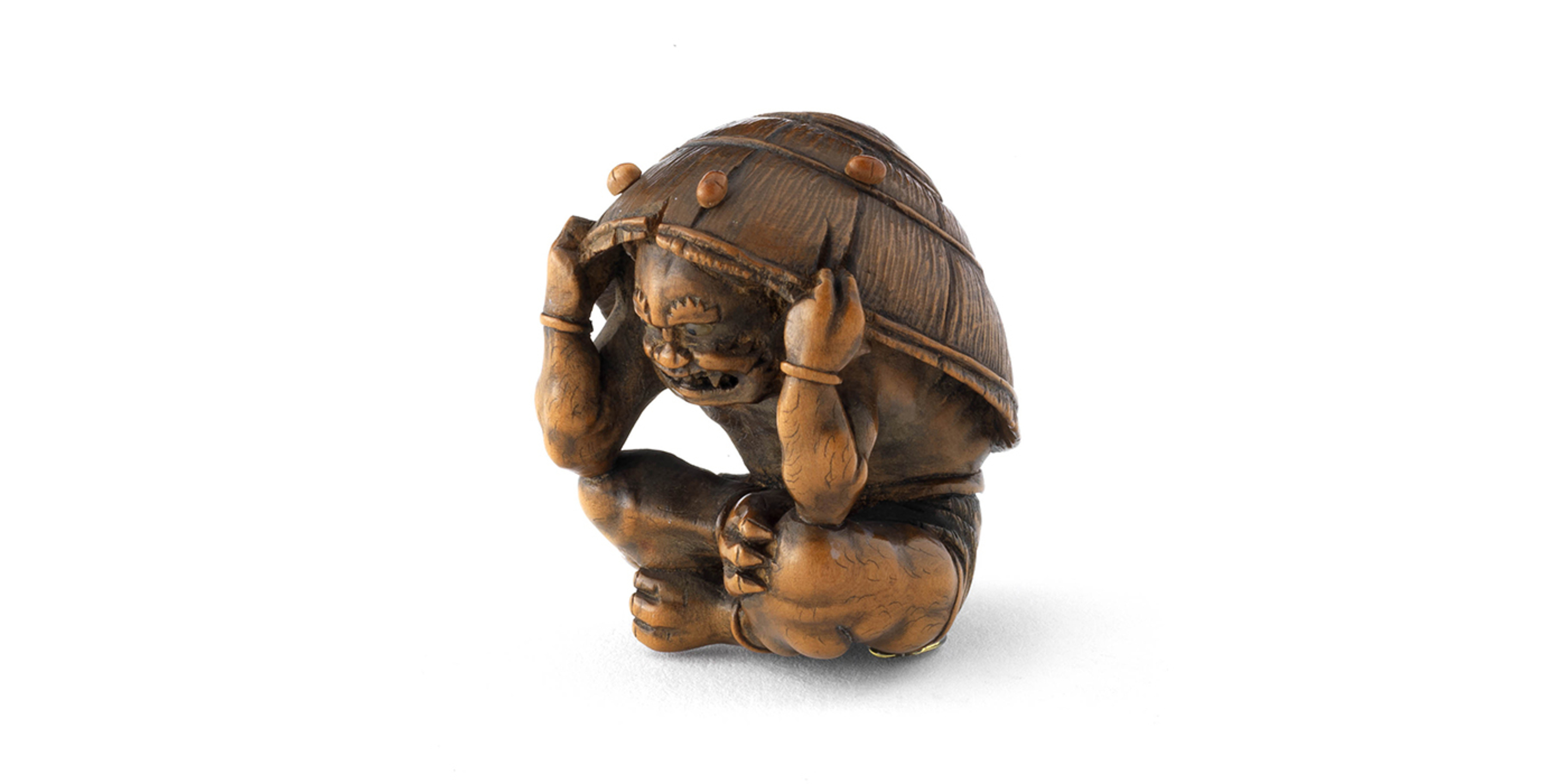 Netsuke / Oni se protégeant sous un chapeau d’une pluie de pois lors de la fête du Setsubun où l’on chasse les démons, Japon, XIX^e siècle. © © musée des Tissus – Pierre Verrier
